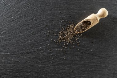 Tahta kaşıkta Chia tohumları. Siyah arka planda sağlıklı keten süper yiyecekler. Taş üzerinde Salvia Hispanica antioksidan tanecikleri.