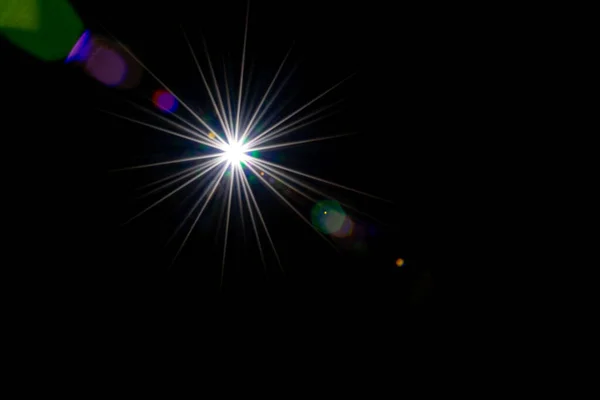 Fondo llamarada. Rayo de luz solar efecto flash en negro. El punto de estrella o el sol brillan con luz brillante en la lente. Brillos redondeados y formas hexagonales, halo arco iris — Foto de Stock