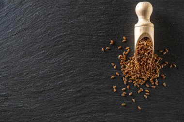 Keten tohumu koyu arka planda izole edilmiş. Kahverengi keten tohumu, keten tohumu taşındaki ahşap kepçeyle organik yağ için keten tohumu. Sağlıklı atıştırmalık: Çiğ vejetaryen atıştırmalık konsepti.