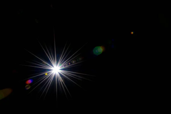 Resplandor efecto de rayos de sol sobre fondo negro. Luz solar destello del punto o luz de la estrella brillan en la lente. Luces bokeh abstractas y reflejo óptico de fugas . — Foto de Stock