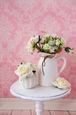 Klasik desenli pembe bir arka planda, eski bir masanın üzerindeki kumaş çiçekler..