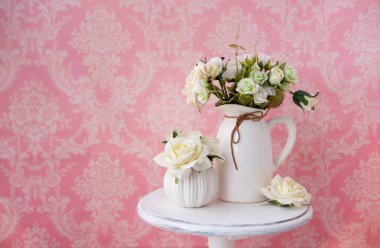 Klasik desenli pembe bir arka planda, eski bir masanın üzerindeki kumaş çiçekler..