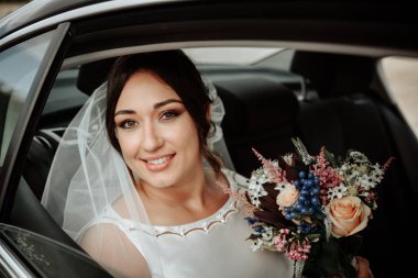 Gülümseyen genç gelin düğün arabasında bir buket çiçekle