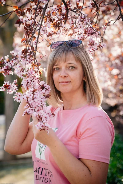 Mooie jonge vrouw in de buurt van de bloeiende roze bloemen lente boom — Stockfoto