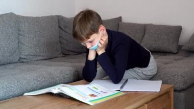 Koronavirüs salgını maskesiyle evde karantinaya alınmış bir çocuk. Uzaktan eğitim ve öğrenme. Kendini izole et, ev karantinası. Dünya Krizi COVID-19. Evde uzaklık öğrenimi