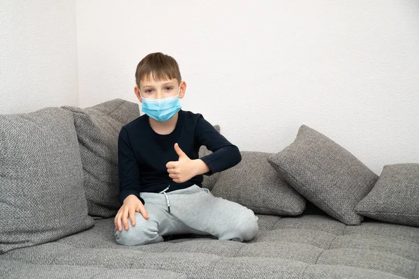 Un niño contento está sentado en una máscara en casa en cuarentena. Mostrar OK, está bien. Epidemia de coronavirus COVID19. Lugar para su mensaje de texto. Cuarentena infantil en casa aislada. Autoaislamiento . —  Fotos de Stock