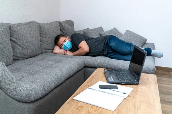 Karantina altındaki tıbbi maskeli adam yorgun ve kanepede uyuyor. Kişisel izolasyon salgını COVID19