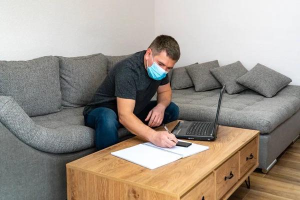 Quarantine coronavirus COVID19 distance job. Young businessman in home quarantine working with laptop in mask. Office man freelancer having conversation on cell phone while working from home