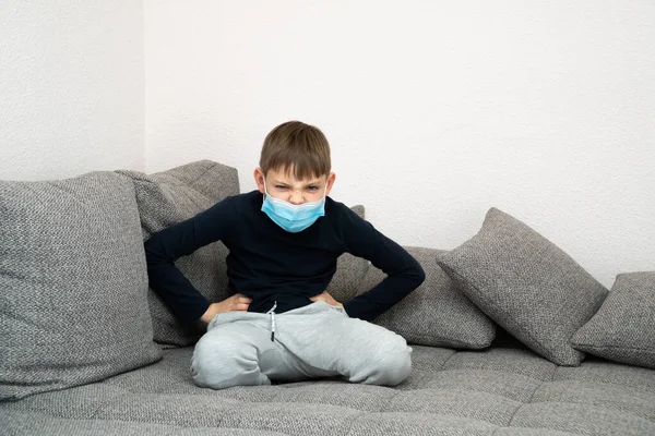 El chico enojado ofendido se sienta en una máscara en casa en cuarentena. Epidemia de coronavirus COVID19. Lugar para su mensaje. Niño en cuarentena en casa aislado. Autoaislamiento en casa. Lugar para el texto —  Fotos de Stock