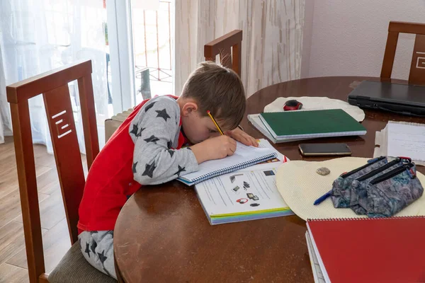 Un niño pequeño estudiando en casa. En la decoración del hogar. Educación a distancia en línea. Un colegial estudia en casa y hace los deberes escolares. Un hogar de aprendizaje a distancia. Cuarentena del Coronavirus . — Foto de Stock