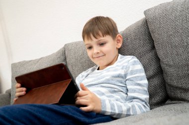 Tablet bilgisayarın önünde düşünen genç bir çocuğa bakıyorum. Uzaktan öğrenme çevrimiçi eğitim. Pandemia Coronavirus karantinasında ev ödevi yapan sevimli beyaz çocuk.