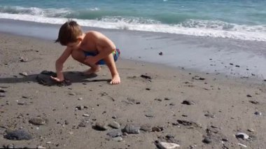 Bir çocuk deniz kenarındaki kuma resim çizer. Cep telefonu videosu
