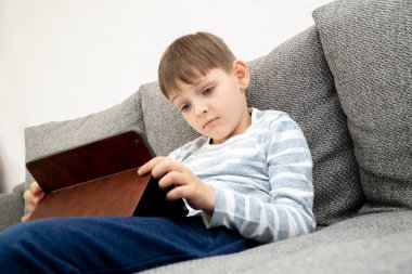 Bir öğrenci tablet kullanarak ders çalışıyor. Bir çocuk tabletteki bir kanepede oturur. Uzaklık öğrenimi çevrimiçi eğitim.