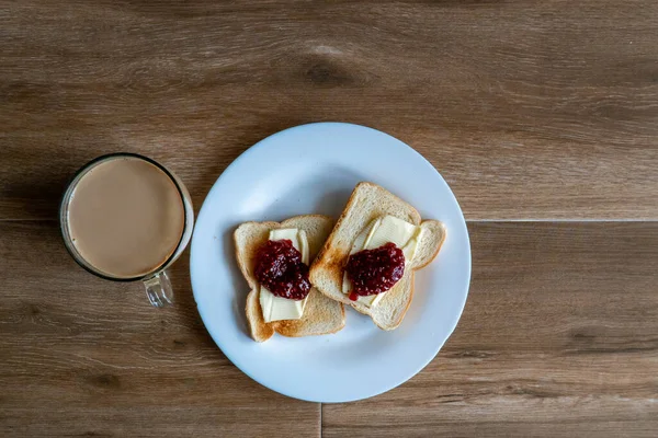 Sütlü bir fincan kahve ve tereyağı ve ahududu reçelli iki dilim kızarmış sandviç. Kahveyle kahvaltı. Metin için boş alan. Üst görünüm.