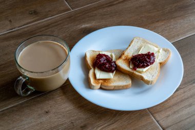 Sütlü bir fincan kahve ve tereyağlı ve ahududulu iki dilim kızarmış sandviç. Kahveyle kahvaltı. Metin için boş alan. Yan görünüm.