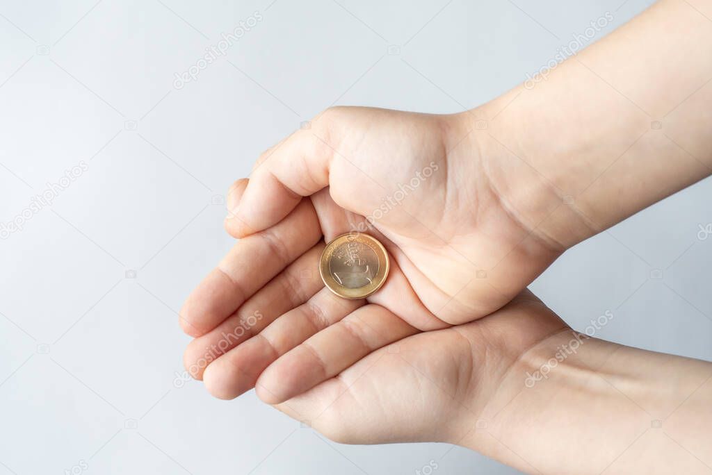 Finance crisis after coronavirus COVID19. Closeup childs hands holding One Euro coin isolated on white background, human hands and saving money concept.