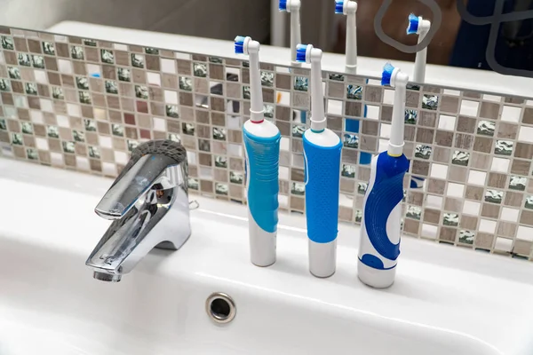 Tres cepillos de dientes eléctricos en el lavabo . — Foto de Stock