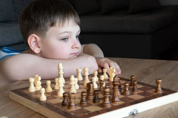 The serious child lost in thought playing chess. Playing board games, on coronavirus quarantine. The child playing chess.