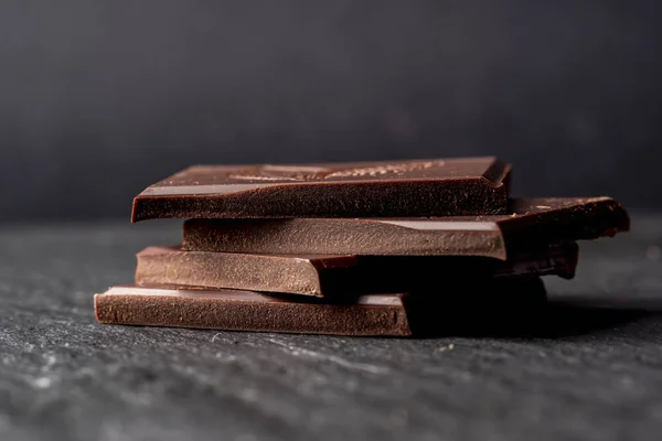 Gebroken stukjes pure bittere chocolade op zwarte stenen ondergrond. — Stockfoto