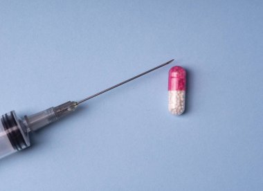 Colored pharmaceutical capsules and syringe. Blue background.