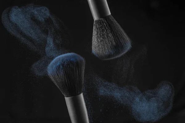 Cosmetic brush with pastel blue cosmetic powder on a black background. Motion freeze — Stock Photo, Image
