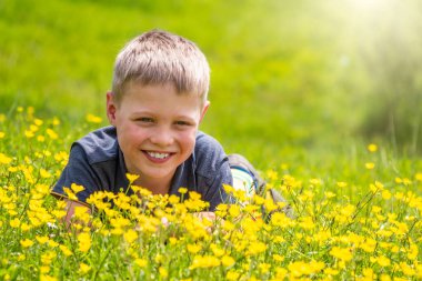 Gülümseyen bir çocuk yeşil çimlerde dinleniyor sarı kır çiçekleriyle gün ışığında