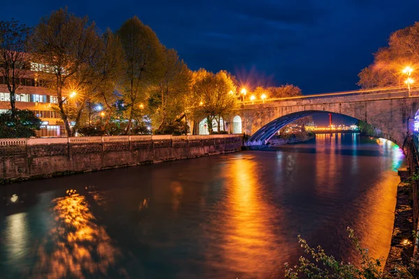 Blick auf die steinerne Brücke über den Fluss bei Nacht mit Lichtstrahlen und Reflexionen — Stockfoto