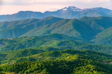 Gün batımında sis içinde dağların katmanları. Dağlarda güzel gün batımı. Ovalarda köyler ve sis ile tepelik bir vadide güzel gün batımı.