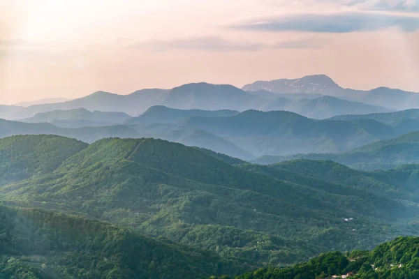 Camadas de montanhas na névoa durante o pôr do sol. Belo pôr do sol nas colinas e montanhas. Belo pôr do sol em um vale montanhoso com nevoeiro nas planícies . — Fotografia de Stock