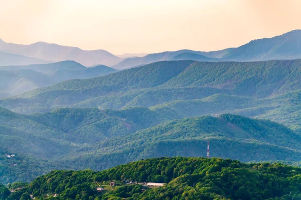 Schichten von Bergen im Dunst während des Sonnenuntergangs. wunderschöner Sonnenuntergang in den Bergen. wunderschöner Sonnenuntergang in einem hügeligen Tal mit Dörfern und Nebel im Tiefland. — Stockfoto