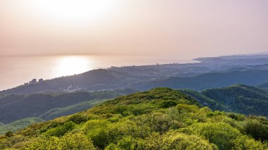 Deniz kıyısı olan yeşil vadi ve güneş altında Soçi şehri. Dağların ve denizin katmanları gün ışığının altında sisli..