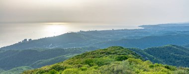 Deniz kıyısı olan yeşil vadi ve güneş altında Soçi şehri. Dağların ve denizin katmanları gün ışığının altında sisli..