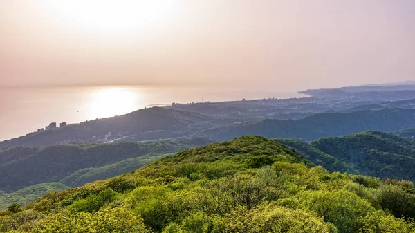 Πράσινη κοιλάδα με την παραλία και την πόλη Σότσι στον ήλιο. Στρώματα των βουνών και της θάλασσας σε μια ομίχλη στο φως της ηλιοφάνειας. — Φωτογραφία Αρχείου