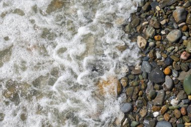 Çakıl taşlı sahilde köpüklü deniz suyu..
