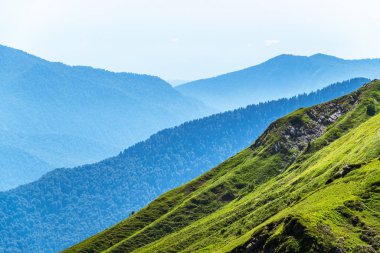 Yeşil dağ sırtları, yüksek dağlarla çevrili. Gün batımında sisli dağların katmanları. Krasnaya Polyana, Sochi, Rusya.