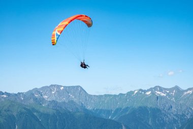 Yeşil Dağ 'ın üzerinde mavi gökyüzünde kırmızı paraglider. Mavi gökyüzünde kırmızı bir paraglider uçuyor.