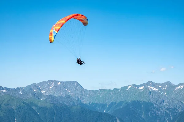 緑の山の上に青空に赤いパラグライダー 青い空に赤いパラグライダーが飛び立つ — ストック写真