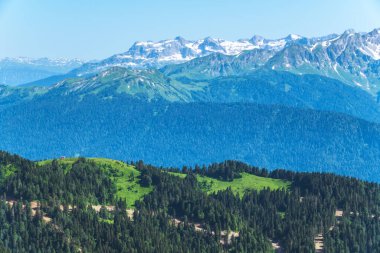 Yeşil dağ sırtları, yüksek dağlarla çevrili. Ufuktaki karla kaplı dağ zirveleri. Gün batımında sisli dağların katmanları. Krasnaya Polyana, Sochi, Rusya.