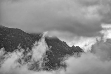 Yoğun bulutların ve sislerin arasına gizlenmiş yeşil yamaçlı yüksek dağ. Bulutlu bir günde dağlarda yoğun sis var. Dramatik bulutlu gökyüzü