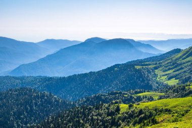 Açık bir yaz gününde yüksek dağlarla çevrili Yeşil Vadi 'ye bakın. Gün batımında sisli dağların katmanları. Çok katmanlı sisli isimler. Krasnaya Polyana, Sochi, Rusya.