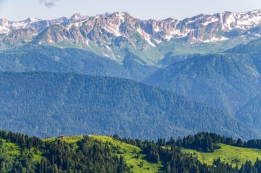Yeşil dağ sırtları, yüksek dağlarla çevrili. Ufuktaki karla kaplı dağ zirveleri. Gün batımında sisli dağların katmanları. Krasnaya Polyana, Sochi, Rusya.