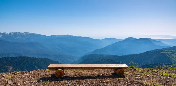 Wooden bench on a mountain range. Beautiful natural landscape, summer mountain landscape over the mountain range with wooden bench and green meadow in nature background.
