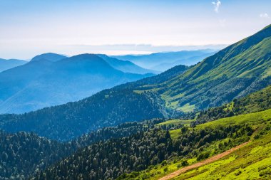 Yaz günbatımında yüksek dağlarla çevrili Yeşil Vadi manzarası. Gün batımında sisli dağların katmanları. Çok katmanlı sisli isimler. Krasnaya Polyana, Sochi, Rusya.