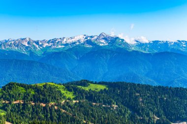 Yeşil dağ sırtları, yüksek dağlarla çevrili. Dağlık bir arazide toprak yol. Ufuktaki karla kaplı dağ zirveleri. Gün batımında sisli dağların katmanları. Krasnaya Polyana, Rusya.