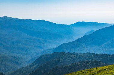 Yaz günbatımında yüksek dağlarla çevrili Yeşil Vadi manzarası. Gün batımında sisli dağların katmanları. Çok katmanlı sisli isimler. Krasnaya Polyana, Sochi, Rusya.