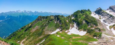 Güneşli bir günde teleferikli kayalık dağın tepesinde. Dağlar, kayalar ve yamaçlarda kar açık mavi gökyüzüne karşı. Yazın kayak merkezinde. Krasnaya Polyana, Sochi, Rusya.