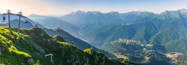 Yaz günbatımında Aibga Dağları 'nın tepesinden kayak merkezi Rosa Khutor' a panoramik manzara. Teleferikli dağlarda güzel turuncu günbatımı. Krasnaya Polyana, Sochi, Kafkasya, Rusya