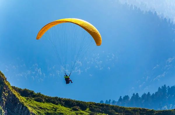 緑の山の斜面の上に黄色のパラグライダー 夏の晴れた日にはパラグライダーが山の斜面を飛ぶ — ストック写真