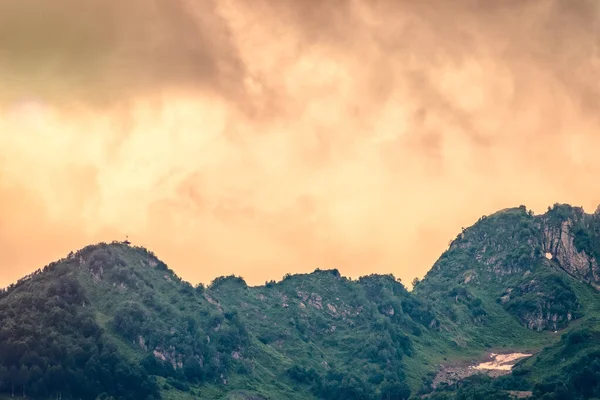 Bulutlu Turuncu Günbatımının Arka Planındaki Yeşil Yamaçta Kalın Bulutlu Dağ — Stok fotoğraf