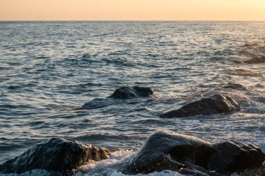 Deniz kıyısında büyük taşlarla portakal rengi günbatımı. Şafak vakti denizin arka planında büyük taşlar. Akşam manzarası kayalık kıyı